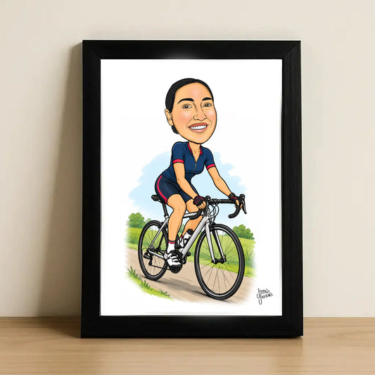 A framed caricature art print of a woman riding a road bicycle, leaning against a light beige wall on a wooden surface. The print features a cartoon illustration of a smiling woman in a navy and red cycling jersey on a white background, enclosed in a black frame.